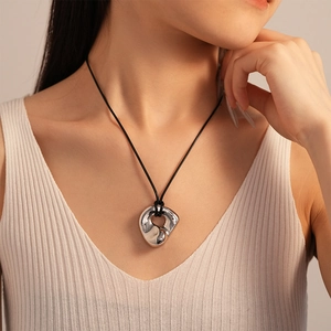 Detail of silver irregular organic pendant on a black cord necklace worn by a model