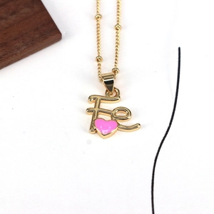 Detail of gold bead chain necklace with Fe letter pendant and pink enamel heart