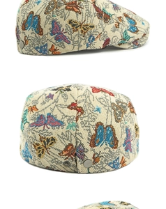 Detail van kleurrijke geborduurde vlinders op een beige jacquard baret met metalen gesp