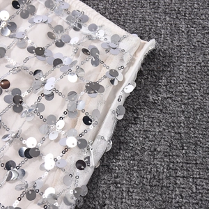 Detailaufnahme des verdeckten Reißverschlusses und silberner Pailletten auf weißem Netzrock