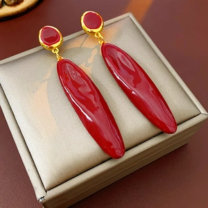 Vue macro de longues boucles d'oreilles goutte en émail rouge et finitions dorées