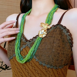 Detail of green beaded multilayer necklace featuring a vintage gold flower clasp on a model