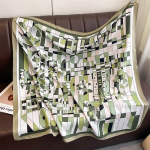 Detail of silk-like scarf with green geometric flower print draped on a leather sofa