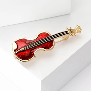 Detailed close-up of a gold and red enamel violin brooch on white geometric blocks