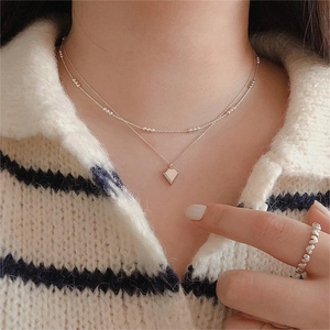 Detail of double-layer silver necklace with geometric pendant and heart-patterned ring