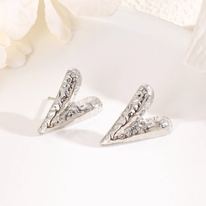 Detailed view of silver heart earrings with textured hammered finish on ceramic tray