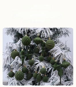 Detail von dunkelgrünen Samt-Weihnachtskugeln mit goldenen Kappen am verschneiten Baum