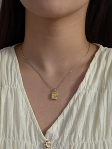 Close-up of elegant silver necklace with square yellow gemstone pendant and zircon accents