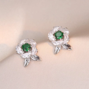 Macro shot of silver flower stud earrings with green emerald center and marquise zircons