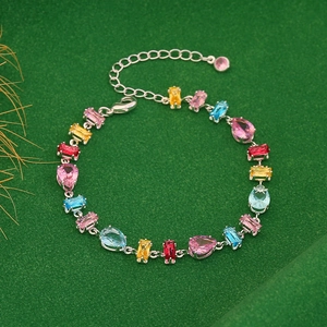 Sparkling silver chain bracelet with colorful pear-cut gemstones on green background