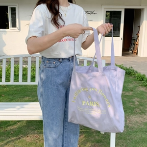 Outdoor lifestyle shot of a purple canvas tote bag with yellow floral Paris embroidery