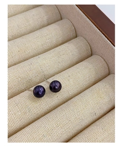 Macro shot of dark purple freshwater pearl earrings set in beige linen jewelry display box