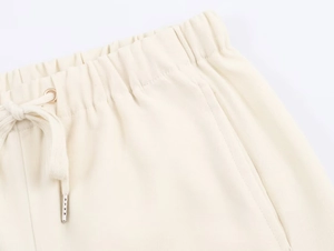 Dettaglio a vita alta elastica con coulisse e punte in metallo su pantaloni bianchi