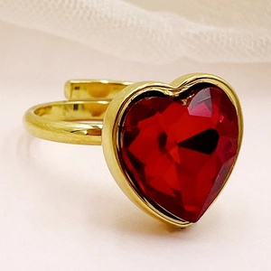 Gros plan d'une bague ajustable dorée ornée d'un zircon en forme de cœur rouge éclatant