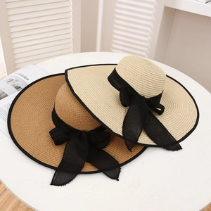 Top view of two wide brim straw sun hats with black ribbons on a white table