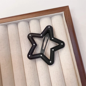 Detail view of a star-shaped black faux leather BB clip with white polka dots and stitching