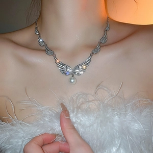 Close-up of angel wing necklace with sparkling zircons and a pearl pendant on a model