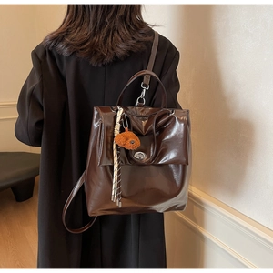 Polished coffee brown leather backpack with silver buckle and dog charm on a model