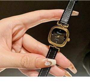 Detailed macro view of a square gold watch with black leather strap on a wrist