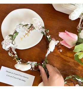 Close-up of white floral headband with realistic silk petals and green leaves on vine