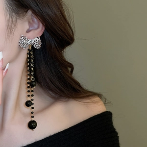 Macro shot of long leopard print bow earrings with black beaded tassels on model
