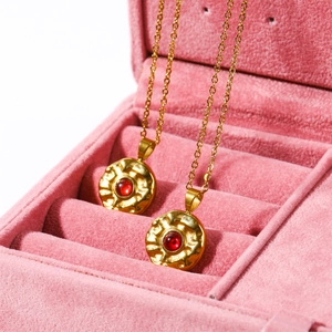 Golden stainless steel coin necklace with red birthstone in a pink velvet jewelry box