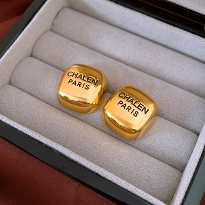 Macro detail of golden square metal stud earrings resting on a grey velvet jewelry box