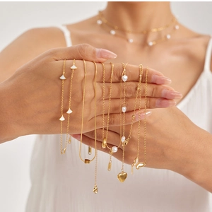 Détail de colliers dorés avec pendentifs cœur, perle et papillon dans un style superposé