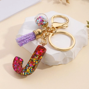 Close-up of resin letter J keychain with colorful sequins, purple tassel, and star charm