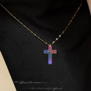 Detailopname van iriserende kruishanger met gouden ketting op zwarte geplooide stof
