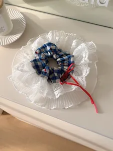 Detail of blue plaid scrunchie with cherry print, white lace edge and red bow decoration
