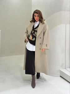 Full-body shot of a long beige double-breasted coat with a vintage brown knit sweater vest