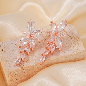 Rose gold flower earrings with marquise zircon crystals on beige stone background