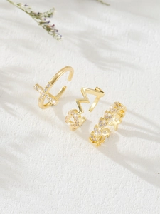 Close-up of three gold-plated rings with zircon cross, heart and floral designs