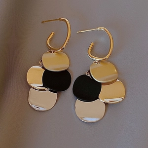 Boucles d'oreilles C dorées avec pampilles de paillettes noires et or sur tissu gris
