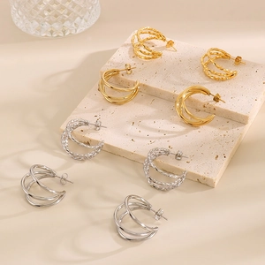 Detail of layered gold and silver C-shaped titanium steel earrings on a beige block