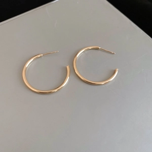 Close-up of minimalist polished golden C-shaped hoop earrings on a grey background