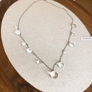 Vue macro d'un collier en acier inoxydable avec perles en résine sur support en tissu beige