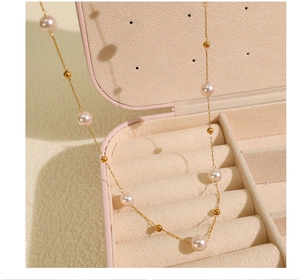 Close-up of pearl and gold bead necklace elegantly draped over a soft pink jewelry box