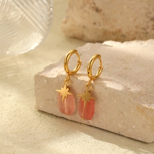Detail view of gold hoop earrings with pink oval stone pendants on beige textured stone