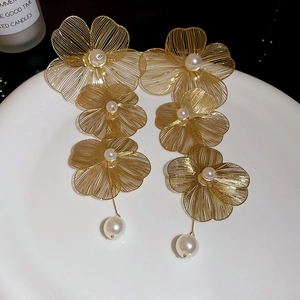 Détail de boucles d'oreilles fleurs dorées tissées avec perles sur plateau céramique
