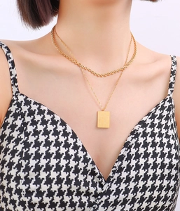 Close-up of a double-layered gold necklace with checkered rectangular pendant on a model