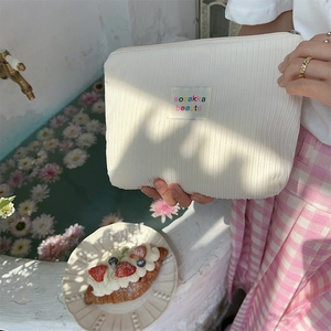 Model holding a cream corduroy cosmetic bag with a small woven label against a resort pool