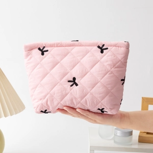 Close-up of pink quilted cosmetic bag with black embroidered bows and metal zipper