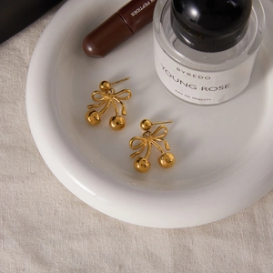 Detail shot of golden bow cherry earrings on a ceramic dish with premium aesthetic