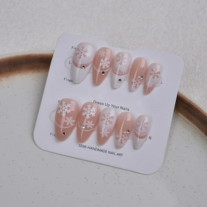 Close-up of almond nails with festive white snowflakes and tiny rhinestone accents