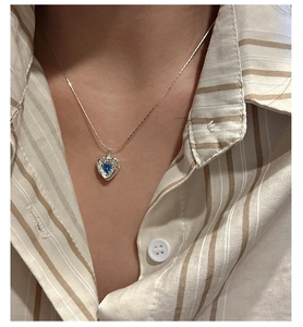 Close-up of S925 silver heart necklace with blue zircon on a beige striped shirt