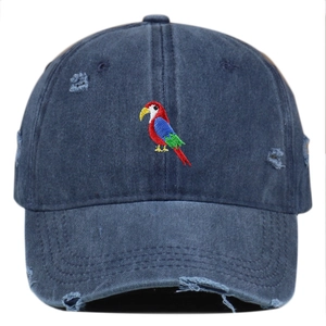 Close-up of colorful parrot embroidery on distressed navy blue washed denim baseball cap