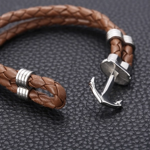 Macro shot of brown leather woven bracelet featuring a polished silver anchor clasp