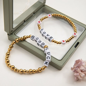 Detail of gold beaded bracelet with LOVE and GOOD LUCK charms in a jewelry box